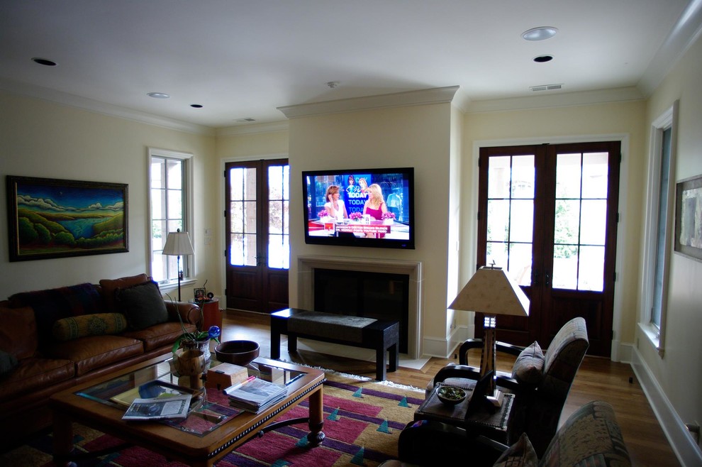 Mittelgroßes Klassisches Wohnzimmer mit gelber Wandfarbe, braunem Holzboden, Kamin, TV-Wand und braunem Boden in Sonstige