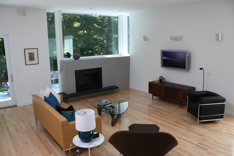 Immagine di un soggiorno moderno con pareti bianche, parquet chiaro, camino ad angolo, cornice del camino in cemento e TV a parete