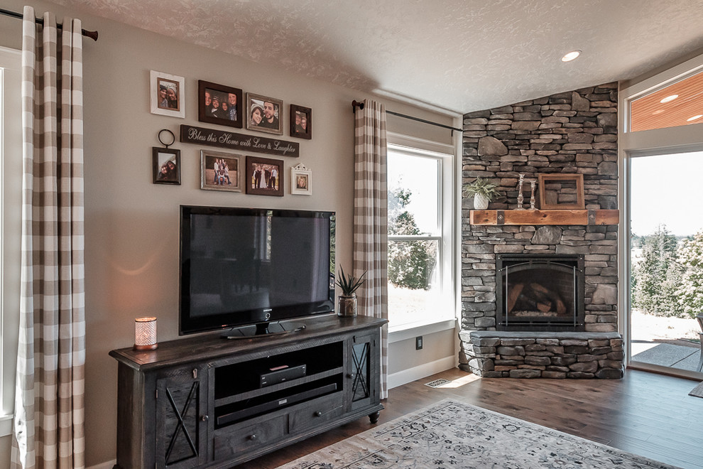 На фото: открытая гостиная комната в стиле рустика с бежевыми стенами, стандартным камином, фасадом камина из камня, отдельно стоящим телевизором и коричневым полом