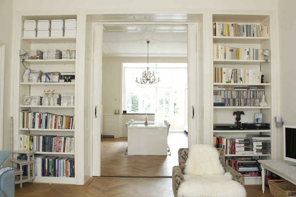 Cette image montre un salon design avec une bibliothèque ou un coin lecture, un sol en bois brun et canapé noir.