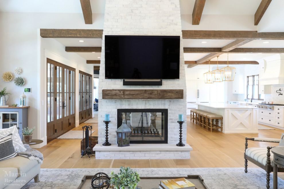 Large farmhouse formal open plan living room in Other with white walls, light hardwood flooring, a two-sided fireplace, a brick fireplace surround, a wall mounted tv and a vaulted ceiling.