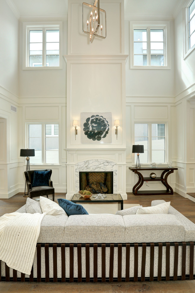 Пример оригинального дизайна: большая парадная, открытая гостиная комната в стиле неоклассика (современная классика) с паркетным полом среднего тона, стандартным камином, серыми стенами и фасадом камина из дерева без телевизора
