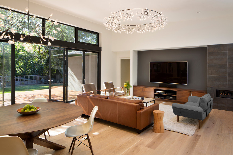 Стильный дизайн: открытая гостиная комната среднего размера в стиле модернизм с серыми стенами, светлым паркетным полом, стандартным камином, фасадом камина из плитки и телевизором на стене - последний тренд