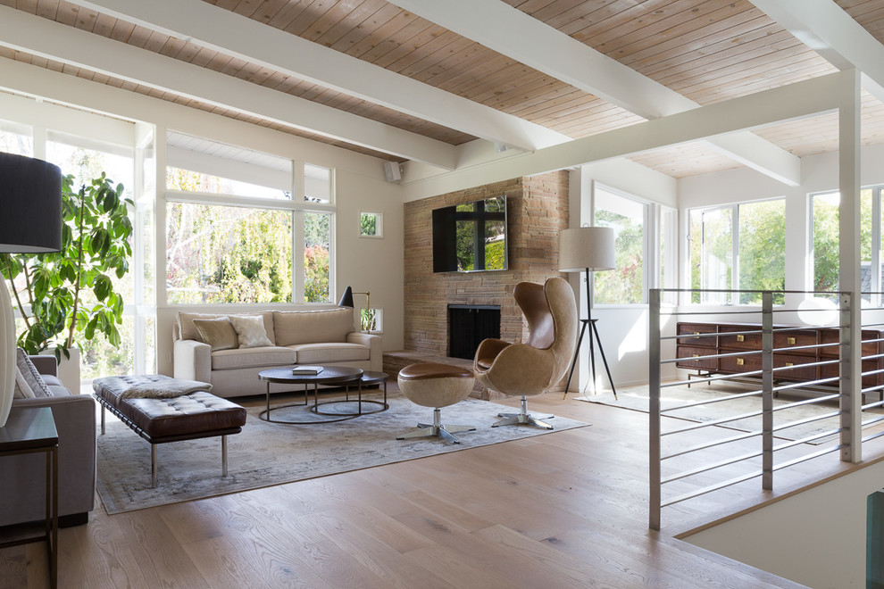 Photo of a large contemporary open plan living room in San Francisco with white walls, light hardwood flooring, a standard fireplace, a stone fireplace surround, a wall mounted tv and brown floors.