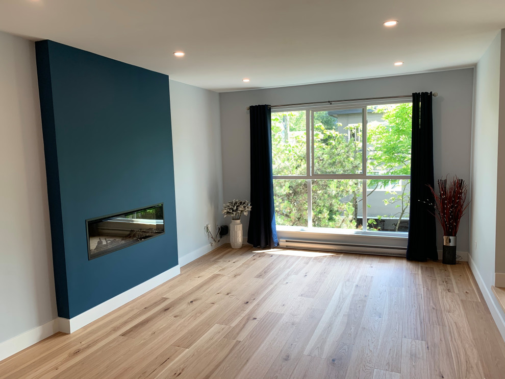 Cette image montre un salon design de taille moyenne et ouvert avec un mur bleu, parquet clair, une cheminée standard, un manteau de cheminée en plâtre et un sol multicolore.