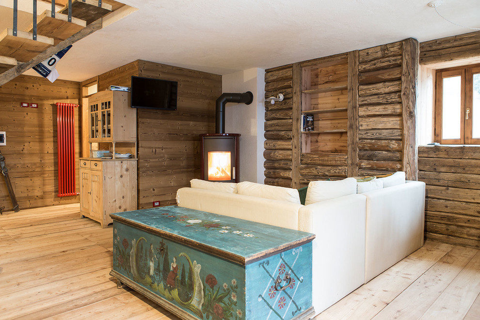 Imagen de salón rústico con suelo de madera clara, estufa de leña y televisor colgado en la pared