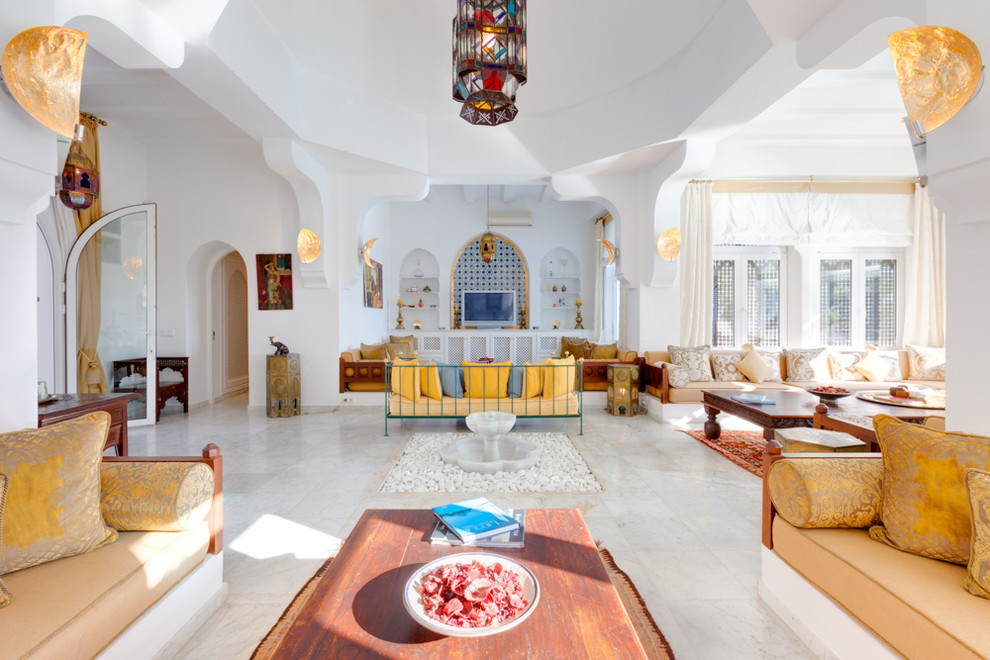 Cette image montre un grand salon méditerranéen ouvert avec une salle de réception, un mur blanc, un téléviseur indépendant, un sol en calcaire et aucune cheminée.