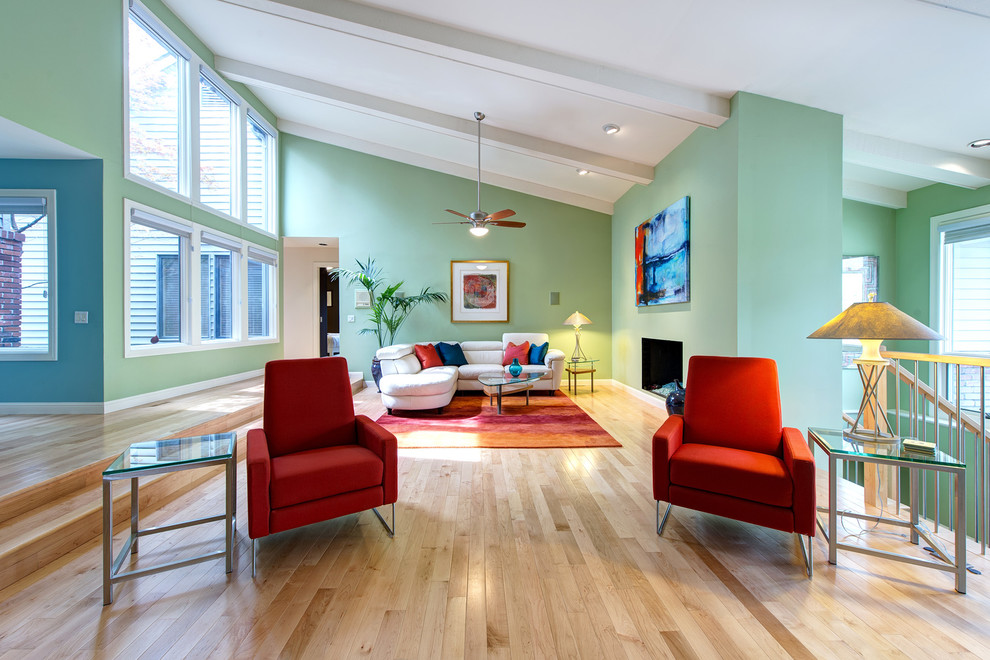 Example of a mid-sized trendy open concept light wood floor and brown floor living room design in St Louis with green walls, a standard fireplace and a plaster fireplace