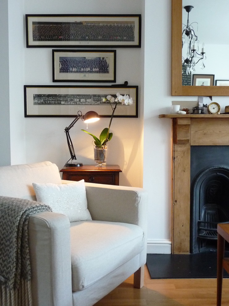Eclectic medium tone wood floor living room photo in London with white walls and a standard fireplace