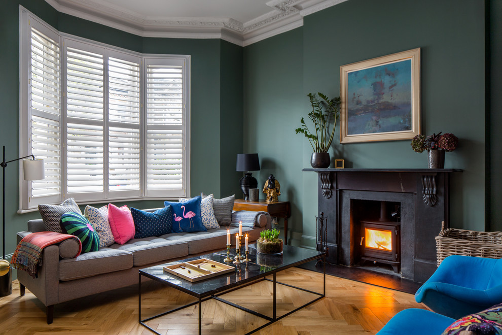 Photo of a bohemian living room in London with green walls, medium hardwood flooring, a wood burning stove and brown floors.