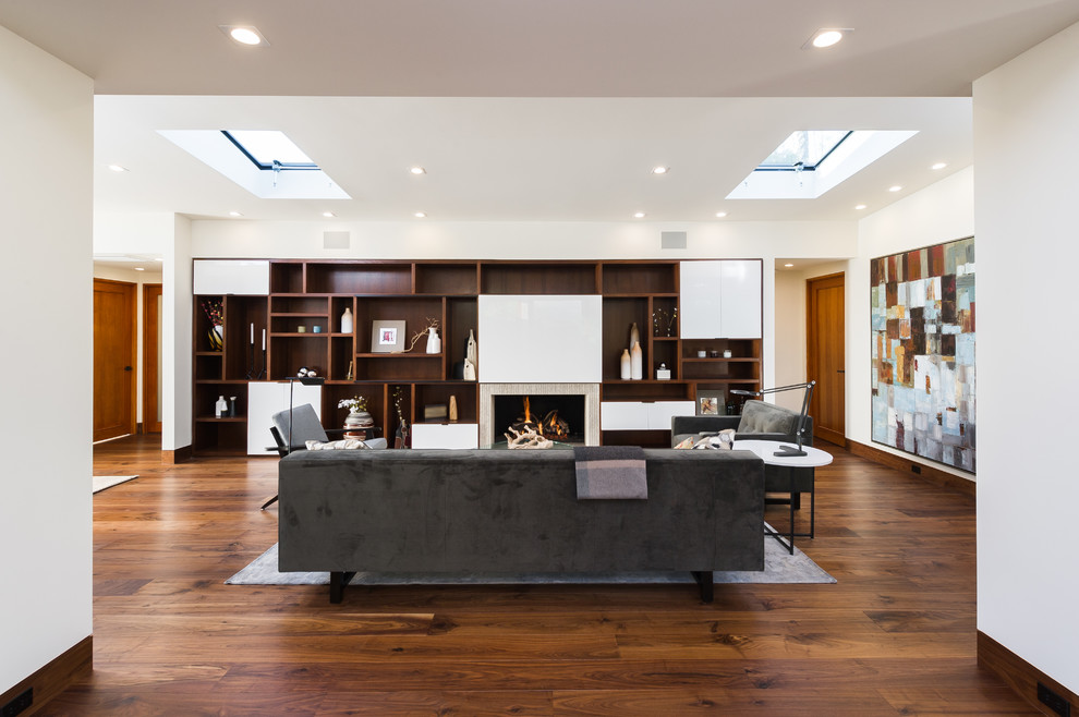 На фото: открытая гостиная комната среднего размера в современном стиле с белыми стенами, паркетным полом среднего тона, стандартным камином, скрытым телевизором, фасадом камина из камня, коричневым полом и ковром на полу