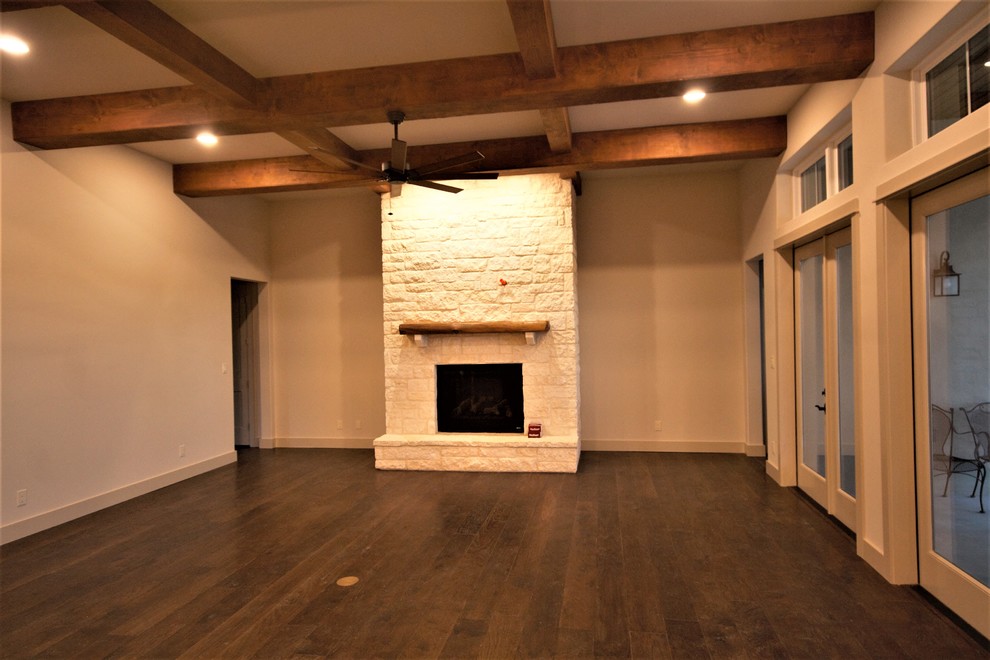 Cette photo montre un salon chic de taille moyenne et ouvert avec une salle de réception, un mur gris, parquet foncé, une cheminée standard, un manteau de cheminée en pierre, un téléviseur fixé au mur et un sol marron.