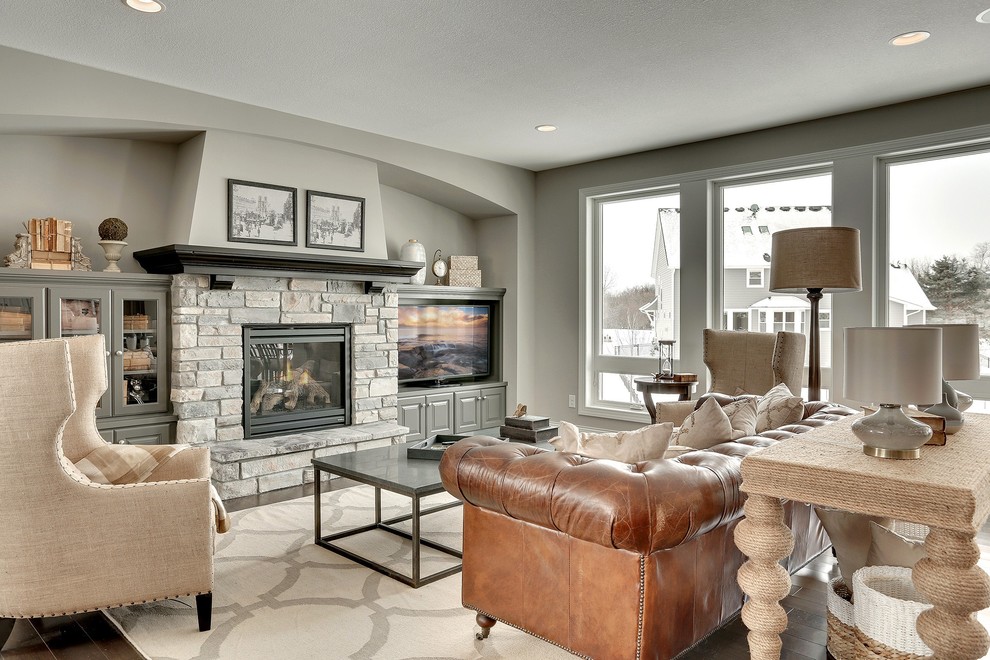 Exemple d'un grand salon chic ouvert avec un mur gris, une cheminée standard, un manteau de cheminée en pierre et un téléviseur dissimulé.