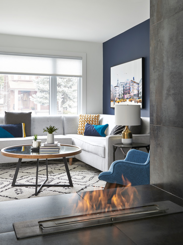 Esempio di un soggiorno moderno di medie dimensioni e aperto con pareti blu, pavimento in legno massello medio, camino bifacciale, cornice del camino piastrellata e TV a parete