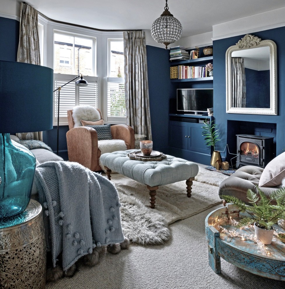 Cette photo montre un petit salon éclectique fermé avec un mur bleu, moquette, un poêle à bois, un manteau de cheminée en brique, un téléviseur encastré et un sol gris.
