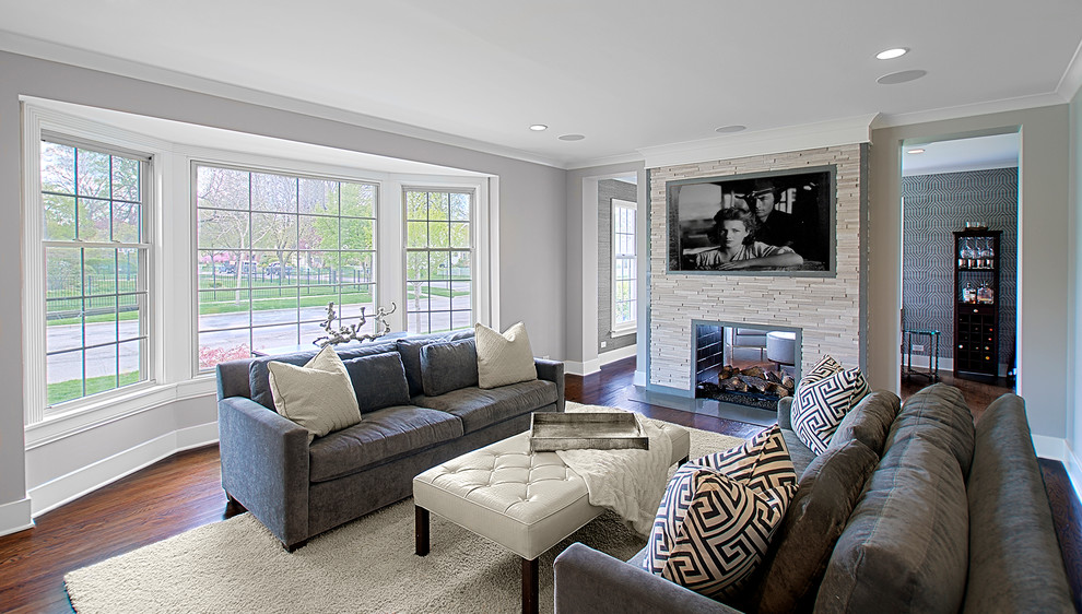 This is an example of a medium sized traditional living room in Chicago with grey walls, dark hardwood flooring, a two-sided fireplace, a tiled fireplace surround, a wall mounted tv and brown floors.