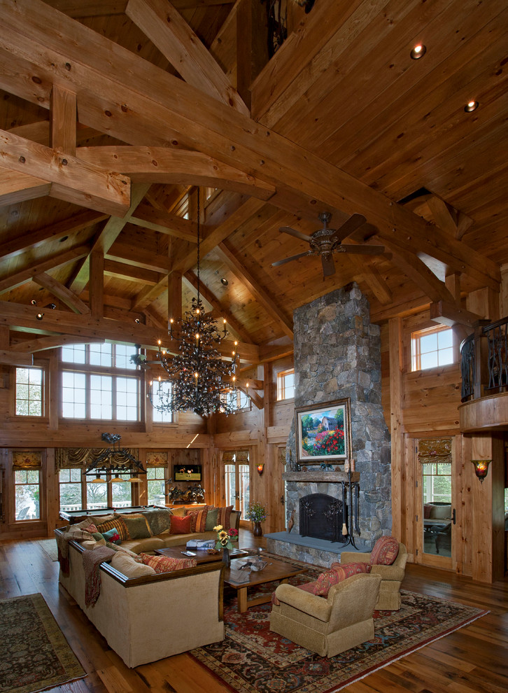 This is an example of an expansive rustic open plan living room in New York with brown walls, medium hardwood flooring, a standard fireplace, a stone fireplace surround and a wall mounted tv.