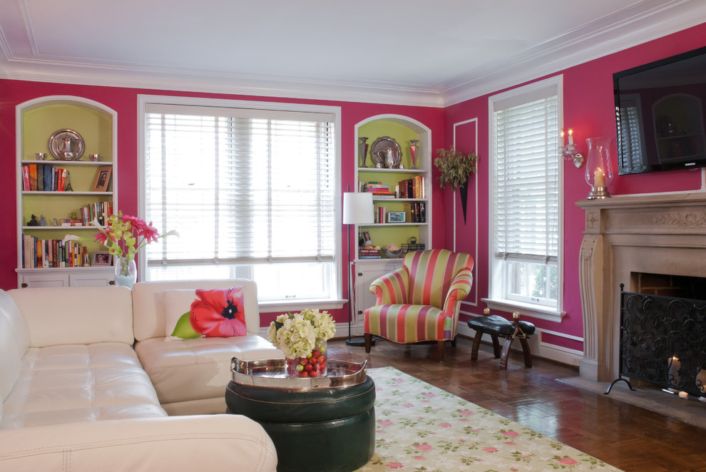На фото: большая открытая гостиная комната в классическом стиле с розовыми стенами, стандартным камином, темным паркетным полом, фасадом камина из бетона, телевизором на стене и коричневым полом