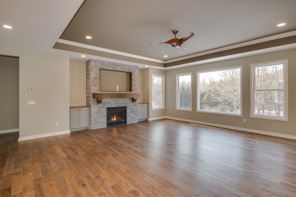 Offenes Wohnzimmer mit beiger Wandfarbe, braunem Holzboden, Kamin und Kaminumrandung aus Stein in Grand Rapids