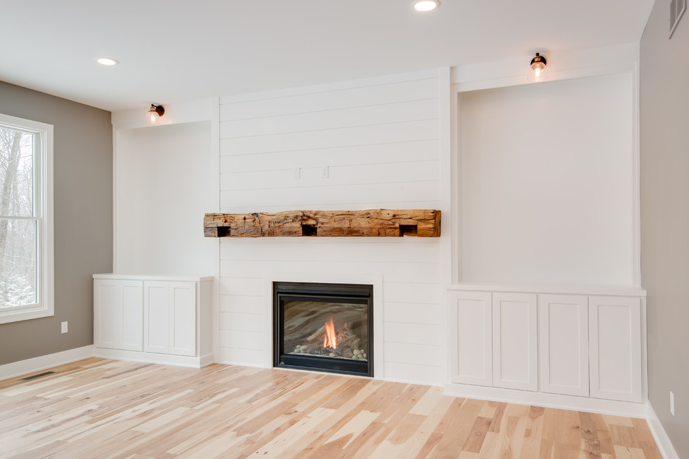 Offenes Wohnzimmer mit weißer Wandfarbe, hellem Holzboden, Kamin und Kaminumrandung aus Holz in Grand Rapids