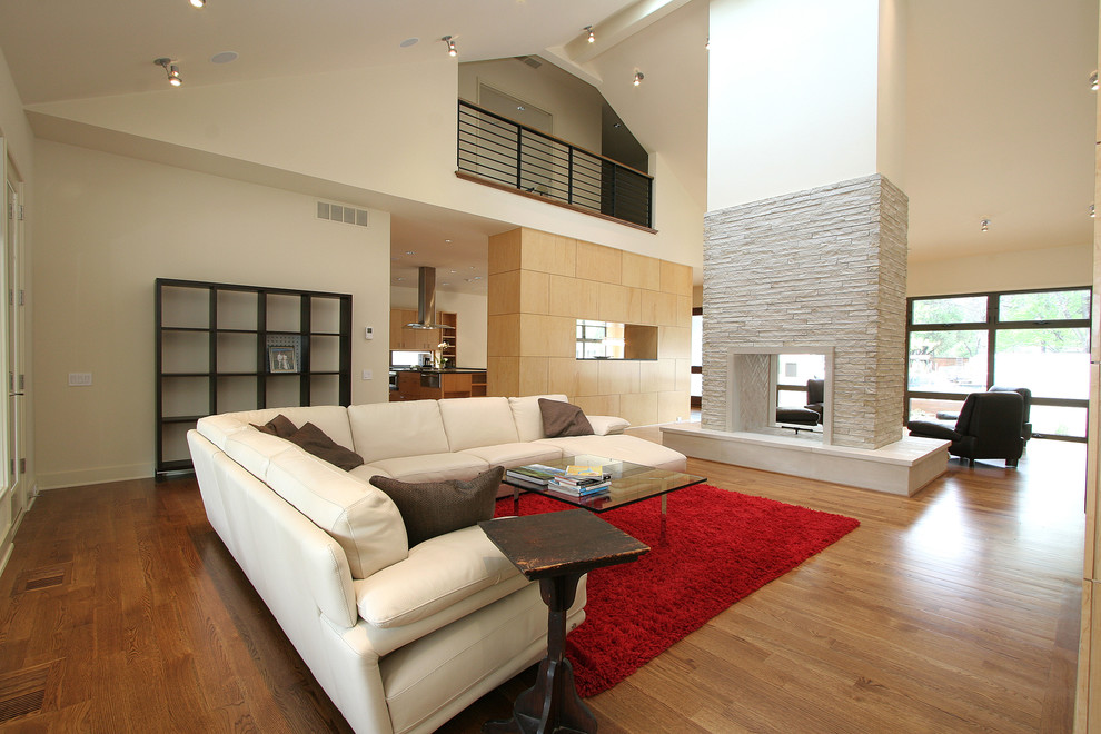 Imagen de salón abierto contemporáneo de tamaño medio con paredes blancas, suelo de madera en tonos medios, chimenea de doble cara, marco de chimenea de piedra y televisor colgado en la pared
