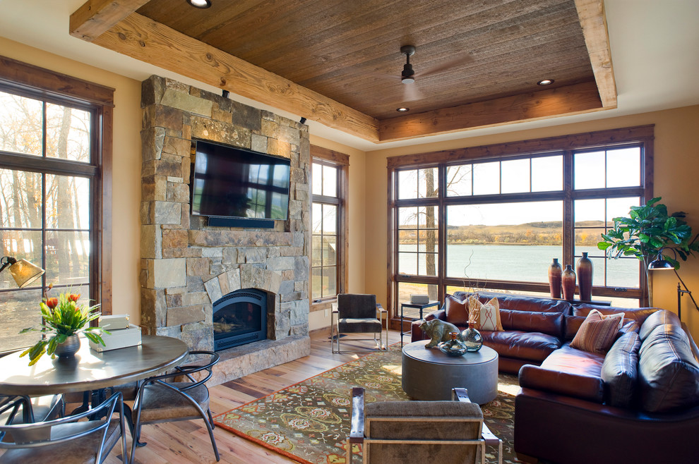 This is an example of a medium sized rustic formal enclosed living room in Other with beige walls, light hardwood flooring, a standard fireplace, a stone fireplace surround, a wall mounted tv and brown floors.