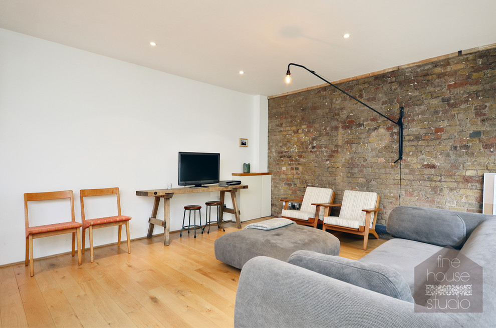 Großes, Offenes Industrial Wohnzimmer ohne Kamin mit weißer Wandfarbe, braunem Holzboden und freistehendem TV in London