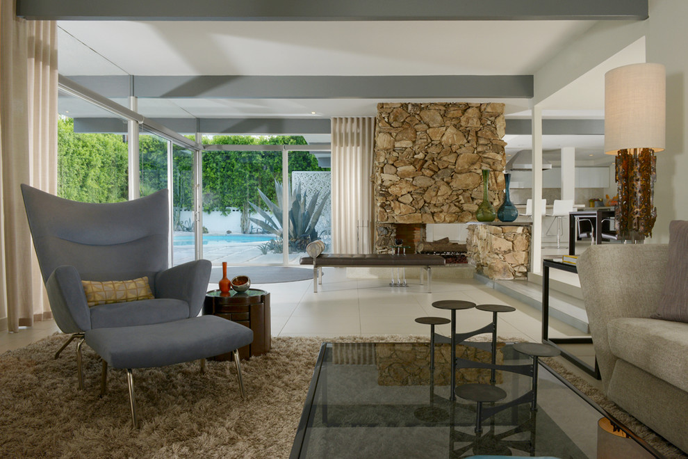 На фото: гостиная комната в современном стиле с белыми стенами, полом из керамогранита, двусторонним камином и фасадом камина из камня с