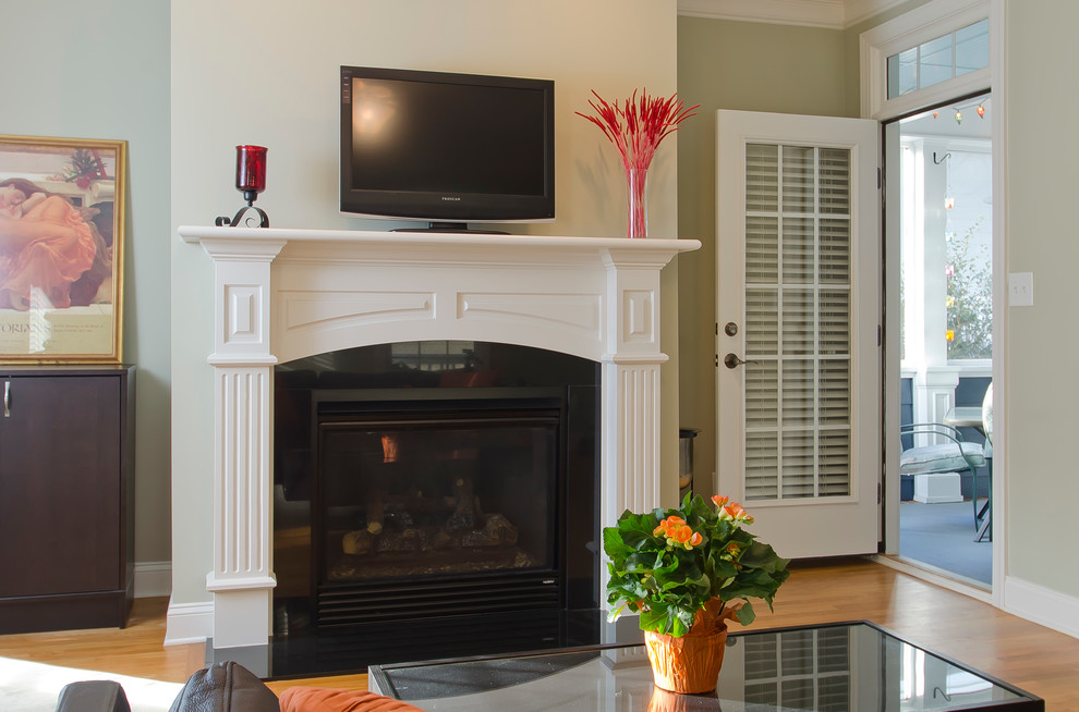 ローリーにあるお手頃価格の小さなトラディショナルスタイルのおしゃれなリビング (茶色い壁、無垢フローリング、標準型暖炉、木材の暖炉まわり、据え置き型テレビ) の写真