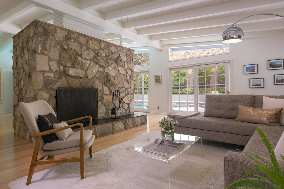 Пример оригинального дизайна: большая двухуровневая гостиная комната в стиле ретро с белыми стенами, полом из керамогранита, двусторонним камином и фасадом камина из камня