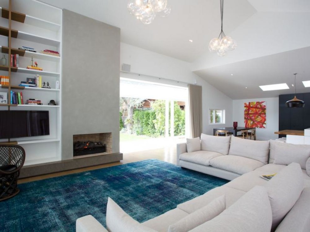 Großes, Offenes Modernes Wohnzimmer mit weißer Wandfarbe, hellem Holzboden, Kamin, Kaminumrandung aus Beton und Multimediawand in Auckland