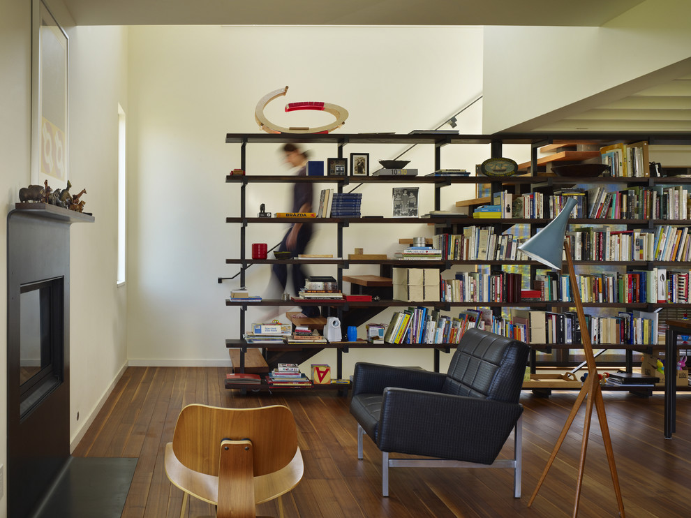 Idee per un soggiorno minimalista di medie dimensioni e aperto con libreria, pareti bianche, pavimento in legno massello medio, camino classico e cornice del camino in metallo
