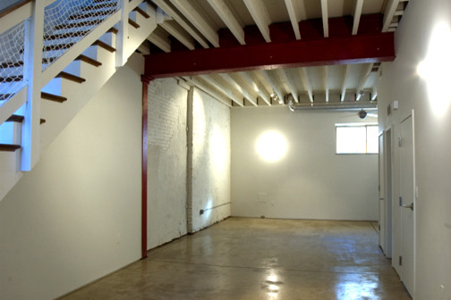 Cette photo montre un salon mansardé ou avec mezzanine industriel de taille moyenne avec un mur blanc, sol en béton ciré, aucune cheminée et aucun téléviseur.