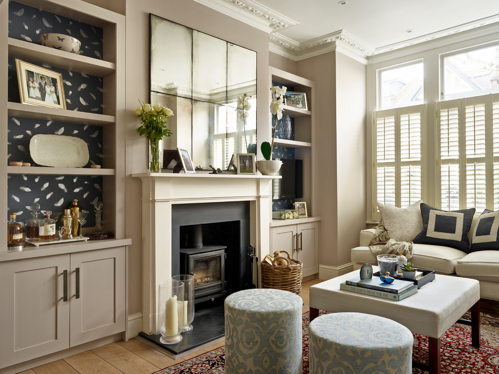 Example of a transitional brown floor and medium tone wood floor living room design in London with a wall-mounted tv, beige walls, a wood stove and a metal fireplace