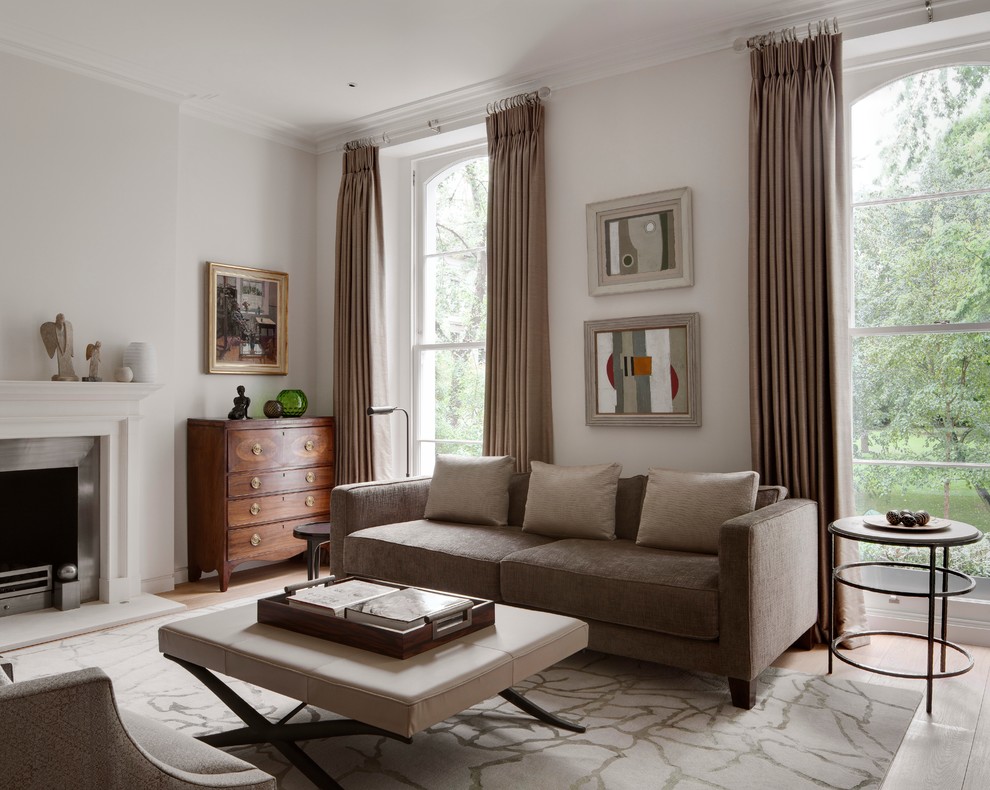 Пример оригинального дизайна: парадная гостиная комната в стиле неоклассика (современная классика) с серыми стенами, светлым паркетным полом, стандартным камином и коричневым диваном без телевизора