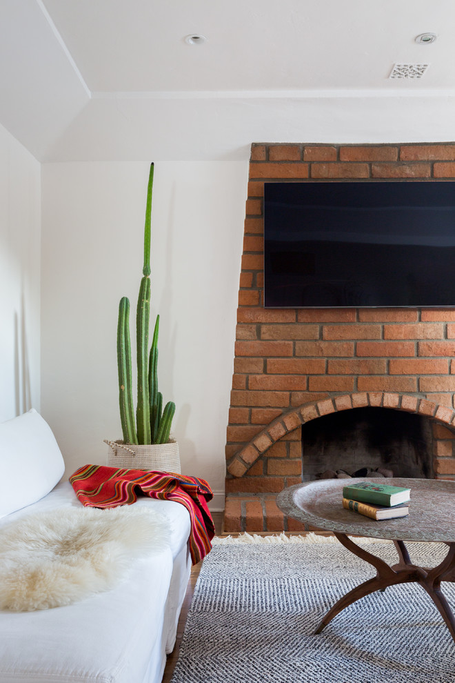 Cette image montre un salon méditerranéen avec un mur blanc, une cheminée standard, un manteau de cheminée en brique et un téléviseur fixé au mur.