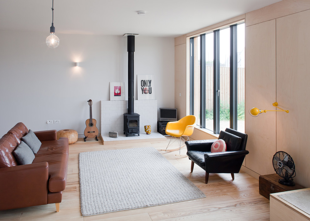 Источник вдохновения для домашнего уюта: открытая гостиная комната в скандинавском стиле с белыми стенами, светлым паркетным полом, печью-буржуйкой, отдельно стоящим телевизором и коричневым диваном