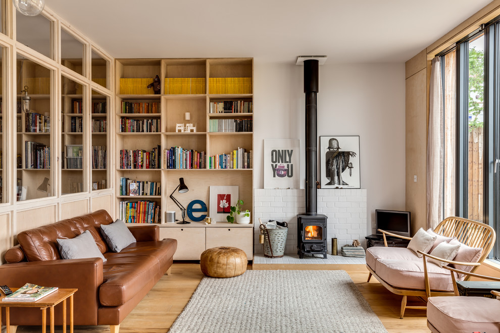 Example of a mid-sized danish open concept light wood floor living room design in London with white walls and a wood stove