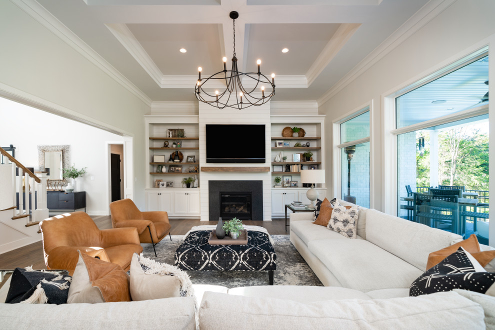 Идея дизайна: открытая гостиная комната в стиле неоклассика (современная классика) с серыми стенами, темным паркетным полом, стандартным камином, телевизором на стене, коричневым полом и многоуровневым потолком