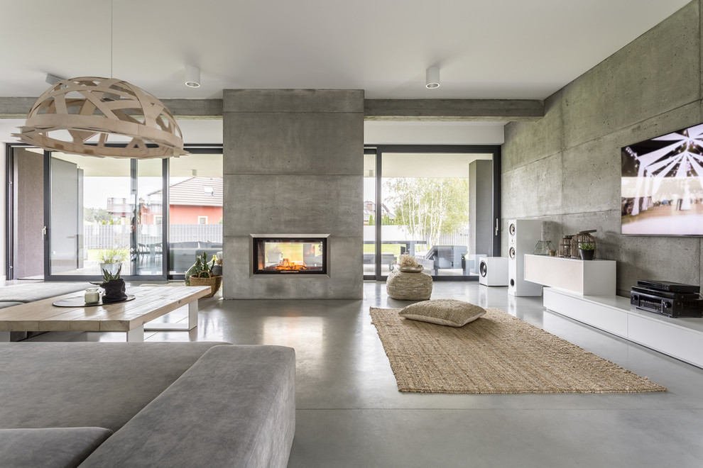 Inspiration pour un très grand salon minimaliste ouvert avec un mur gris, sol en béton ciré, une cheminée double-face, un manteau de cheminée en béton, un téléviseur fixé au mur et un sol gris.