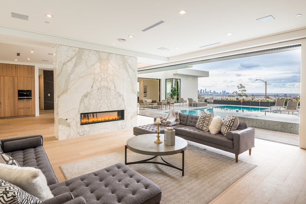 Offenes Modernes Wohnzimmer mit weißer Wandfarbe, hellem Holzboden, Gaskamin, Kaminumrandung aus Stein und beigem Boden in Los Angeles