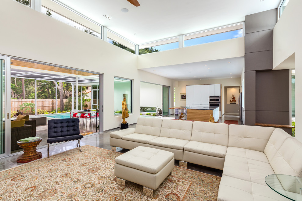 Diseño de salón abierto tropical con paredes blancas, suelo de cemento y televisor colgado en la pared