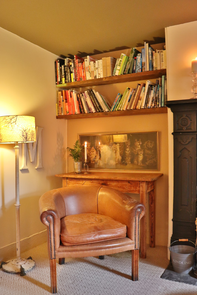 Imagen de biblioteca en casa cerrada clásica renovada pequeña con paredes beige, moqueta, estufa de leña, marco de chimenea de yeso, televisor en una esquina y suelo beige