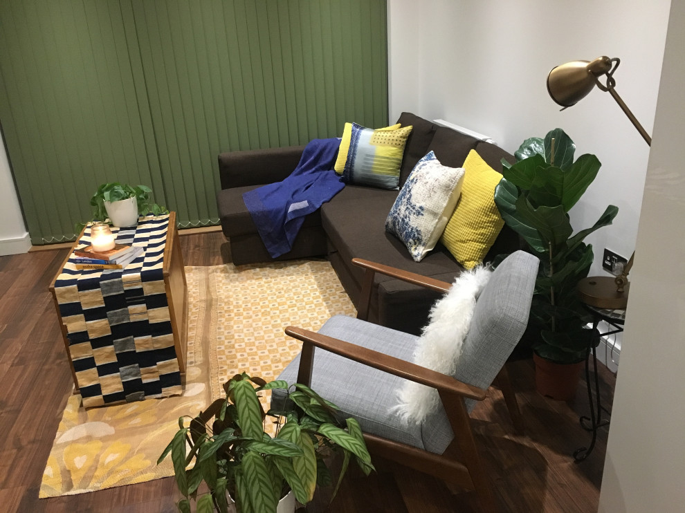 На фото: маленькая гостиная комната в стиле фьюжн с белыми стенами, полом из ламината и коричневым полом для на участке и в саду