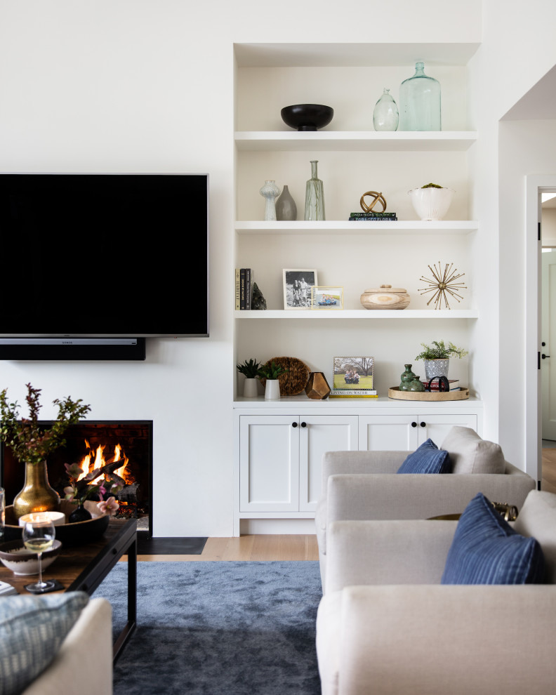 Источник вдохновения для домашнего уюта: большая открытая гостиная комната в стиле неоклассика (современная классика) с белыми стенами, стандартным камином, телевизором на стене и бежевым полом