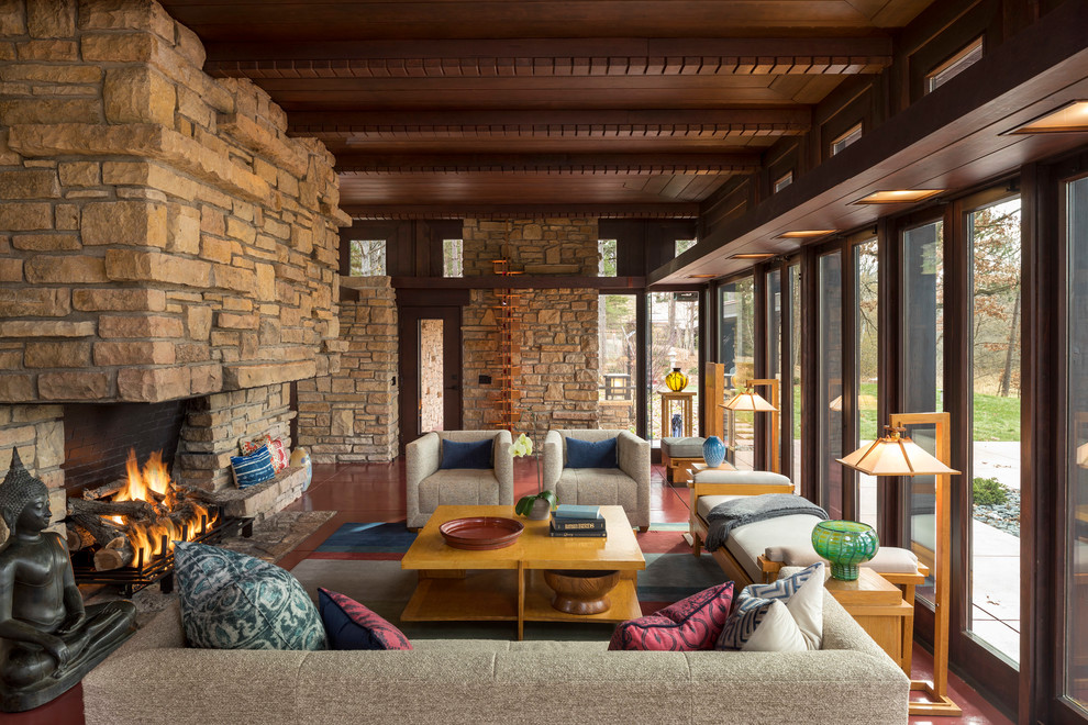 На фото: гостиная комната в стиле рустика с коричневыми стенами, стандартным камином, фасадом камина из камня и красным полом с