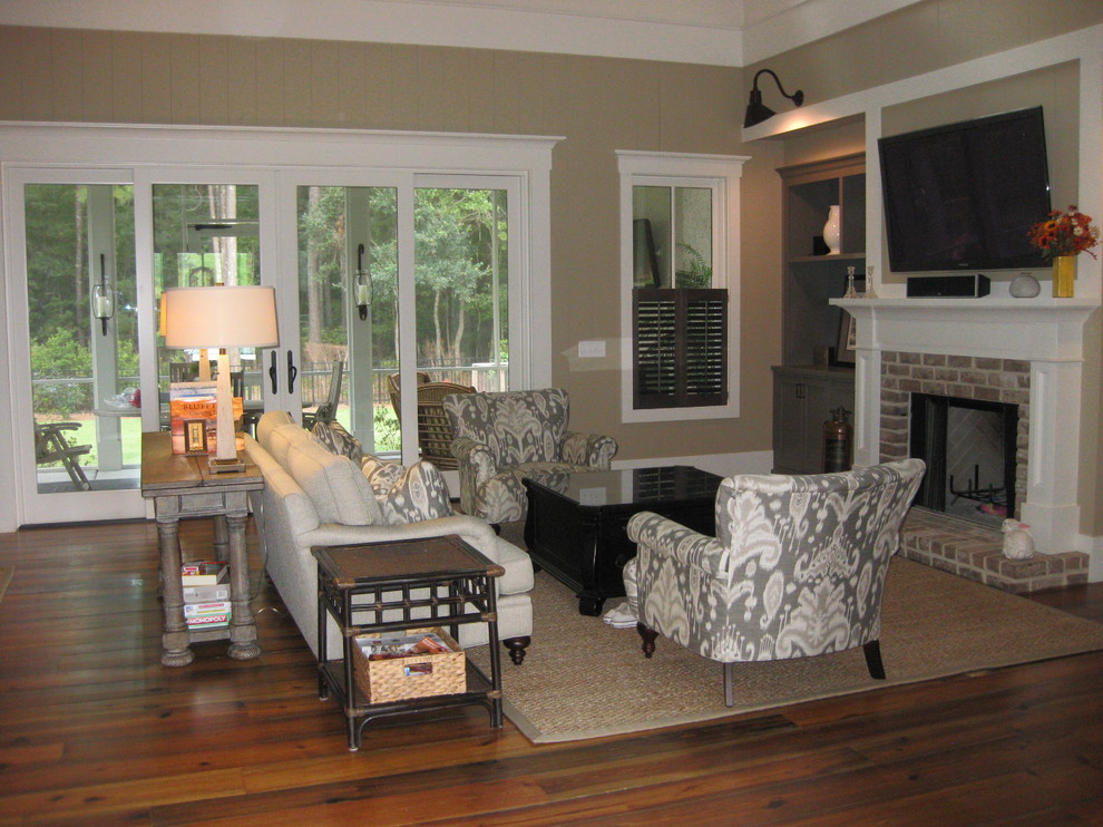Foto di un ampio soggiorno chic aperto con pareti beige, pavimento in legno massello medio, camino classico, cornice del camino in mattoni e TV a parete
