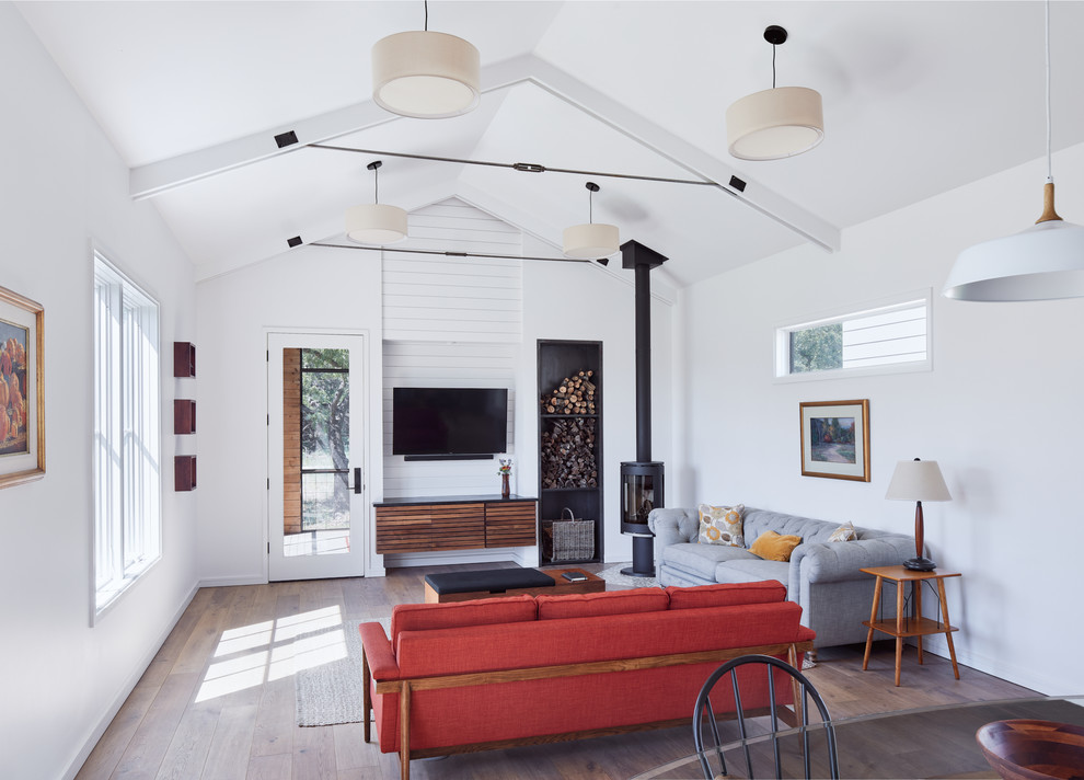Skandinavisches Wohnzimmer mit weißer Wandfarbe, braunem Holzboden, Kaminofen, TV-Wand und braunem Boden in Austin