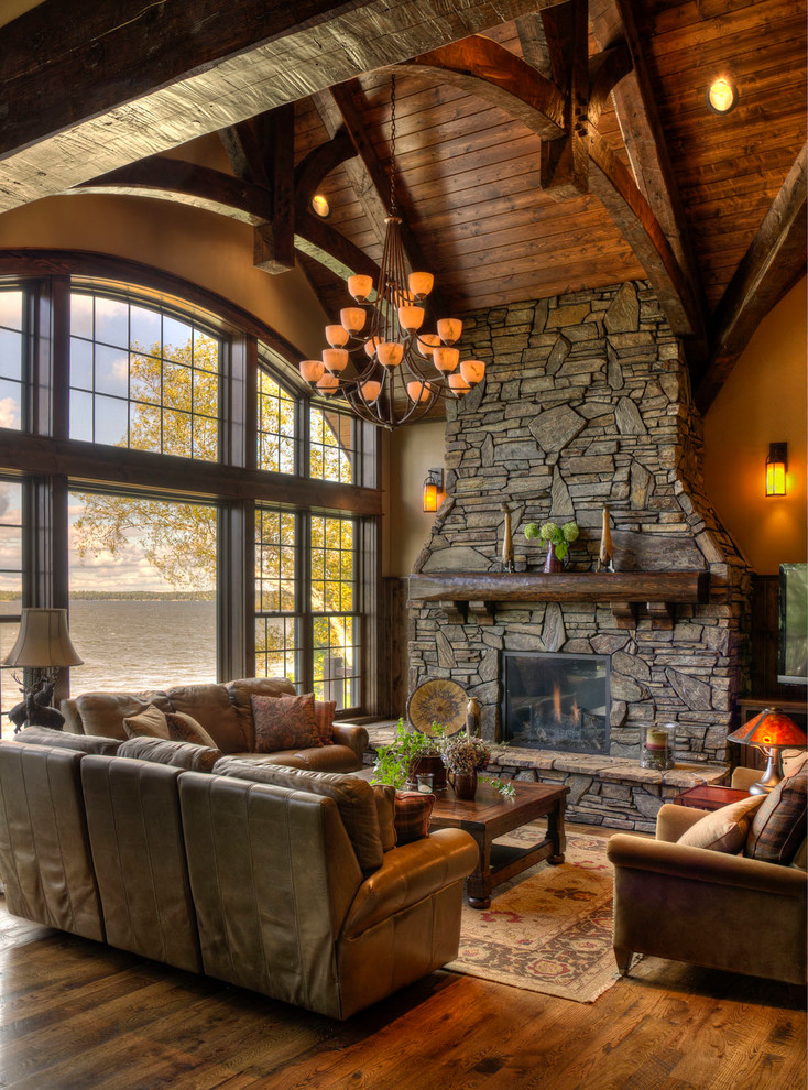 Cette photo montre un salon montagne ouvert avec un sol en bois brun, une cheminée standard et un manteau de cheminée en pierre.