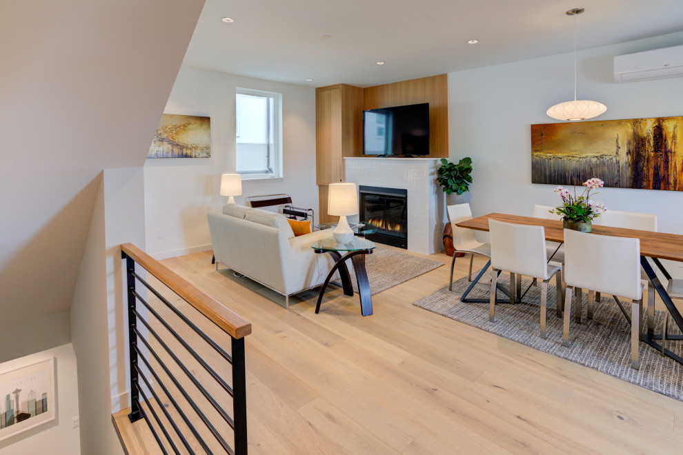Offenes Modernes Wohnzimmer mit weißer Wandfarbe, hellem Holzboden, Kamin, gefliester Kaminumrandung und freistehendem TV in Seattle